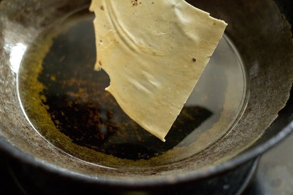 adding papad piece to hot oil in pan for frying. 