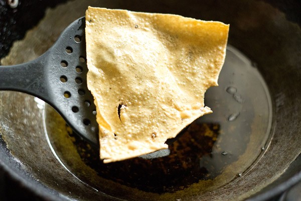 removing fried papad piece from hot oil using a slotted spoon. 
