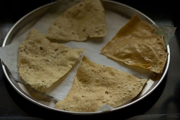 fried papad pieces placed on a kitchen paper towel. 
