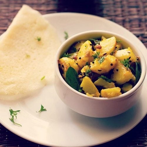potato masala served in a bowl with a dosa on a white plate sprinkled with coriander leaves.