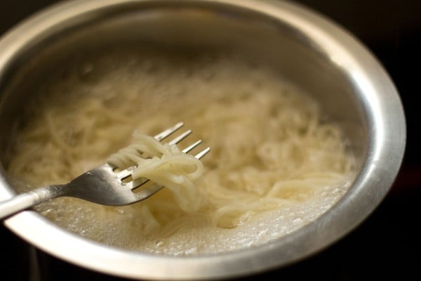 cooked noodles still in water; fork is showing finished consistency