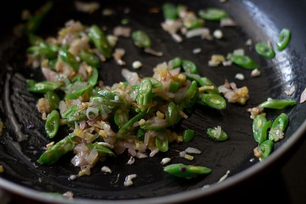 adding sliced beans to the hot wok with onion and garlic