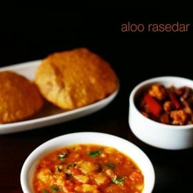 aloo rasedar served in a white bowl with pooris kept on a white platter, mixed veg pickle in a small bowl and text layovers.