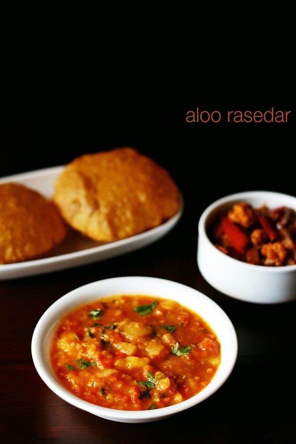 aloo rasedar served in a white bowl with pooris kept on a white platter, mixed veg pickle in a small bowl and text layovers.