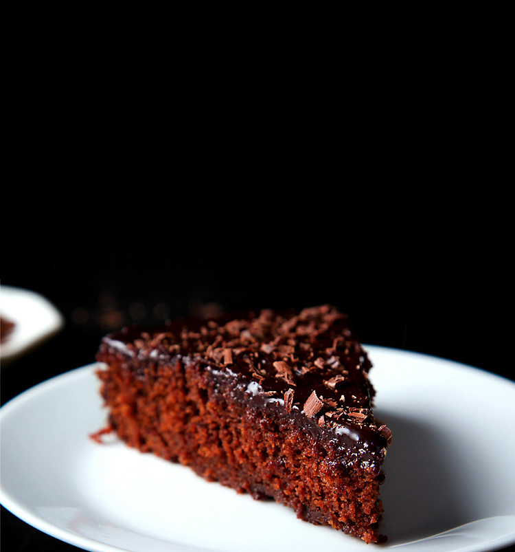 A triangular slice of eggless chocolate cake on a white plate