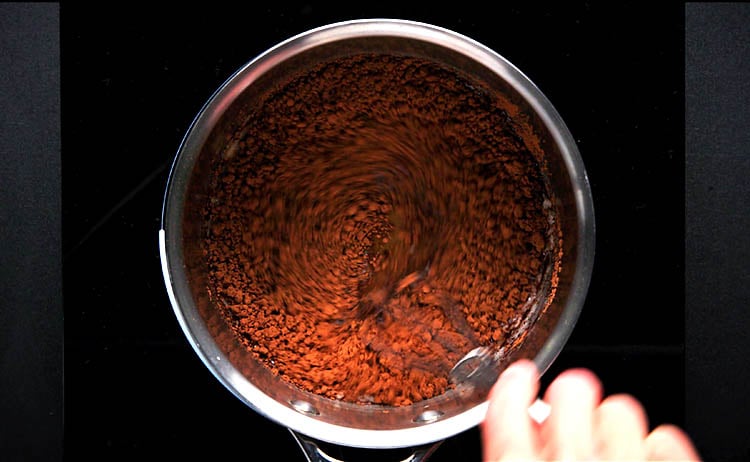 cocoa powder being mixed into milk and sugar mixture with a whisk