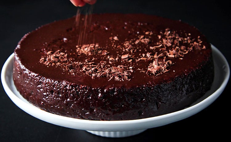 vegan chocolate cake being decorated with chocolate shavings