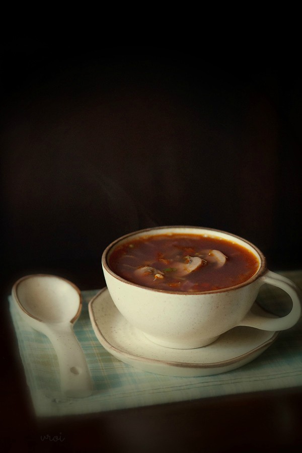 mix vegetable soup in a cream colored ceramic mug placed on top of ceramic plate and a ceramic spoon by side 