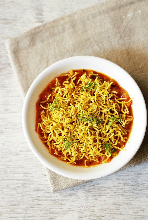 sev tameta nu shaak garnished with sev and coriander leaves and served in a white bowl. 