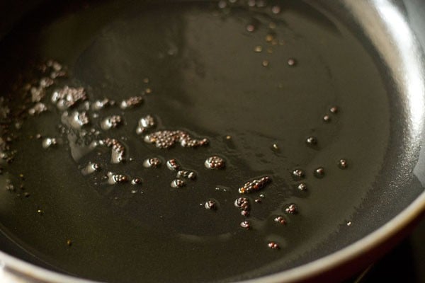 crackling mustard seeds in hot oil in a pan for making sev tamatar sabji. 
