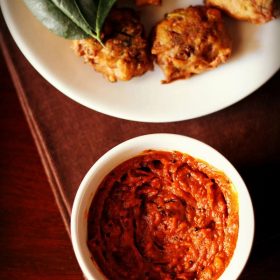 tomato chutney served in a small white bowl with a platter of pakoda kept on the top side and text layover.