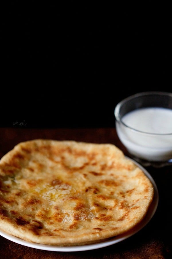 aloo kulcha served on a plate with a bowl of curd by side