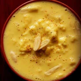 top shot of rabri in red bowl with nuts and a light sprinkle of saffron powder from top.