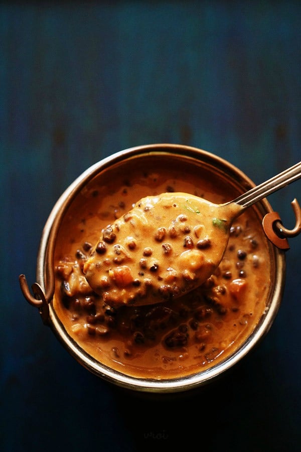 dal makhani served in a small copper bucket and taken in a spoon on a dark blue board. 