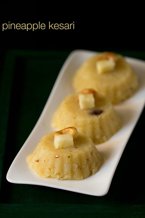 pineapple kesari garnished with fried cashew and pineapple cube and served on a white platter with text layover.