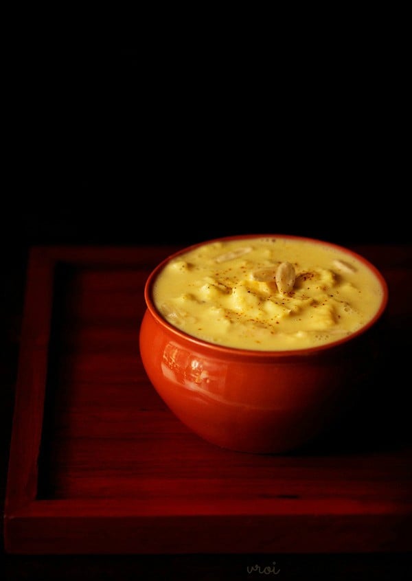 rabri topped with slivered nuts in a red ceramic bowl