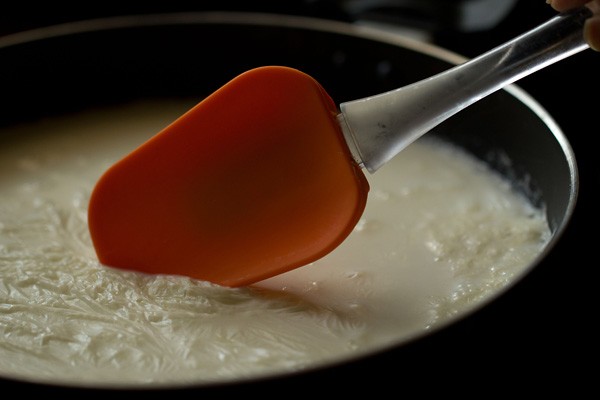 boiling milk with clotted cream layer being moved with orange spatula