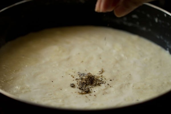 adding cardamom to thickened milk for making rasmalai recipe