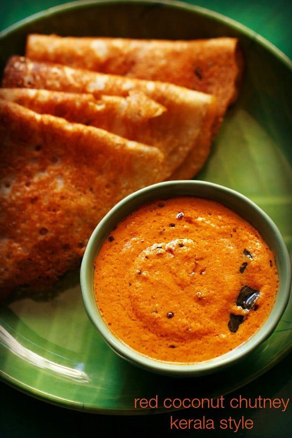 red coconut chutney served in a green colored bowl placed on a green colored plate with folded dosas kept on the upper left side and text layovers.