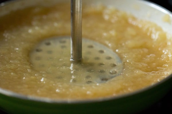 mashing applesauce with potato masher.