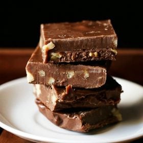 Chocolate fudge squares stacked on top of each other placed on a white plate on a wooden tray.