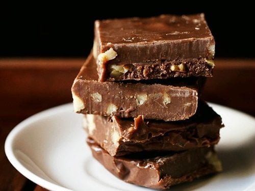 Chocolate fudge squares stacked on top of each other placed on a white plate