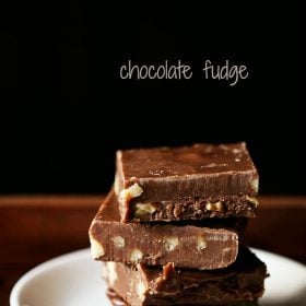 Chocolate fudge squares stacked on top of each other placed on a white plate on a wooden tray.