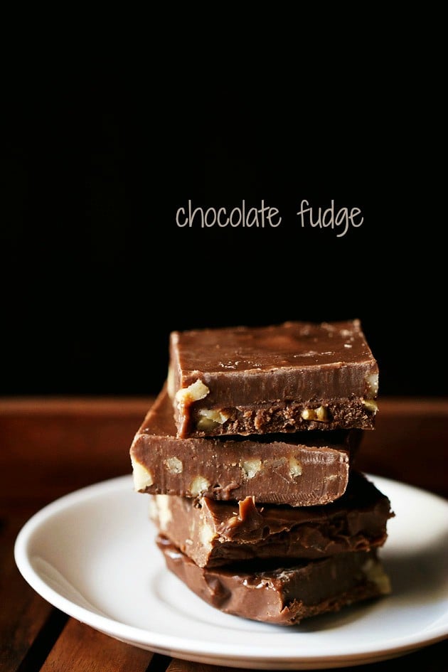 Chocolate fudge squares stacked on top of each other placed on a white plate on a wooden tray.