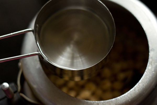 adding water to stovetop pressure cooker having potatoes and chickpeas