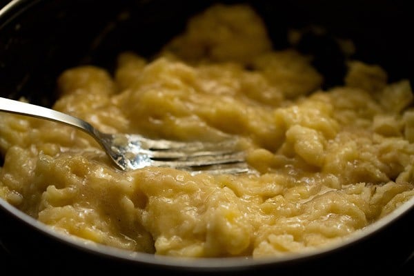 Closeup shot of silver fork crushing bananas in bowl