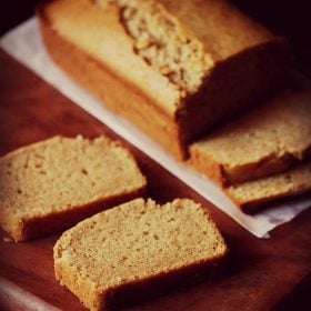 closeup shot of pound cake slice on a brown wooden board with pound cake loaf in the background.