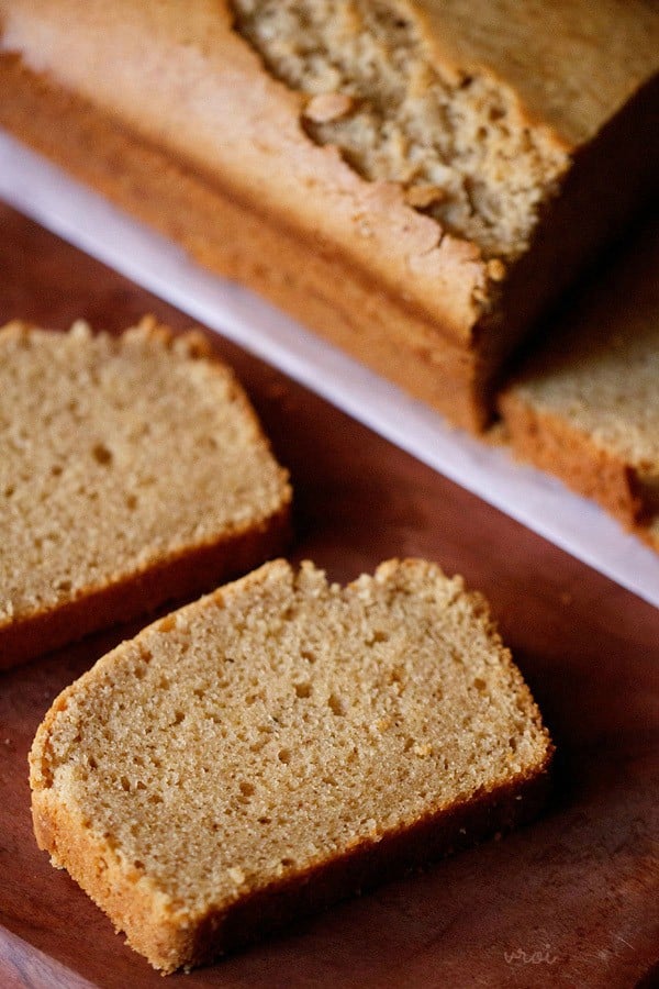 closeup shot of pound cake slice on a brown wooden board with pound cake loaf in the background