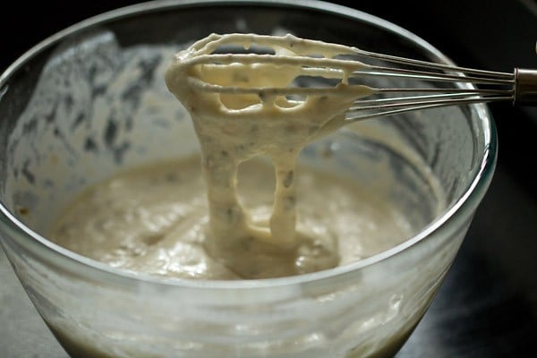 dripping malpua batter off a whisk to show the consistency