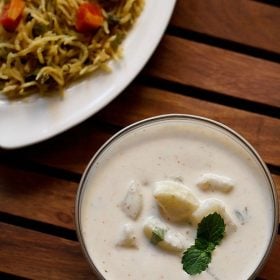 aloo raita garnished with mine leaves and served in a glass bowl with pulao.