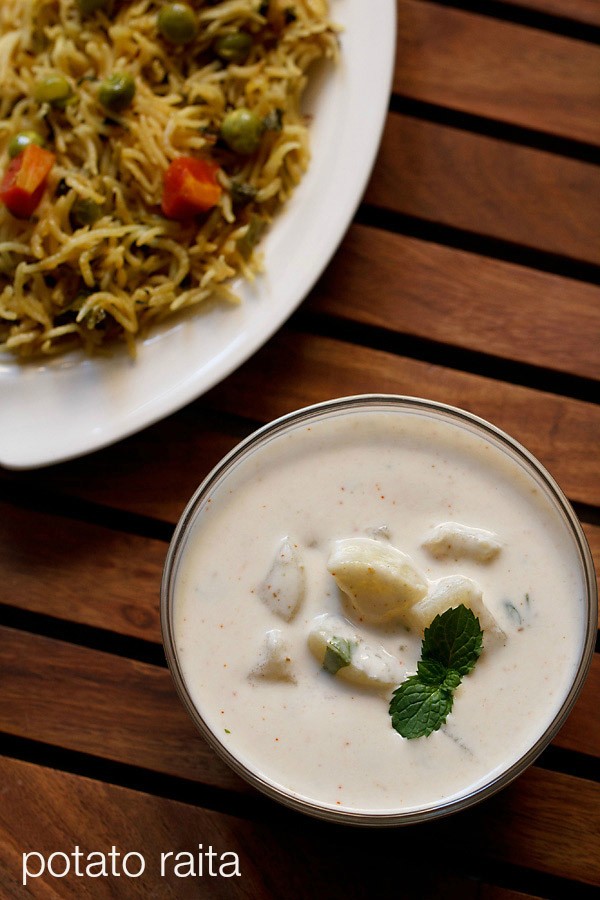 aloo raita garnished with mine leaves and served in a glass bowl with pulao.