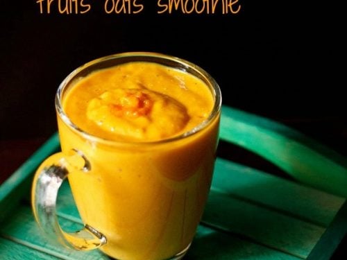 bright orange colored fruit and oatmeal smoothie in a glass mug on a green table.