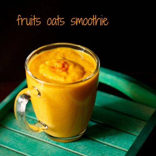 bright orange colored fruit and oatmeal smoothie in a glass mug on a green table.