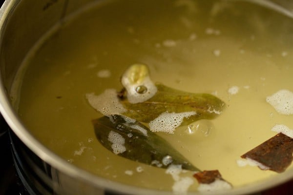 water with whole spices floating on the top in the pan