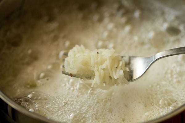 three fourth cooked rice grains being shown with a fork