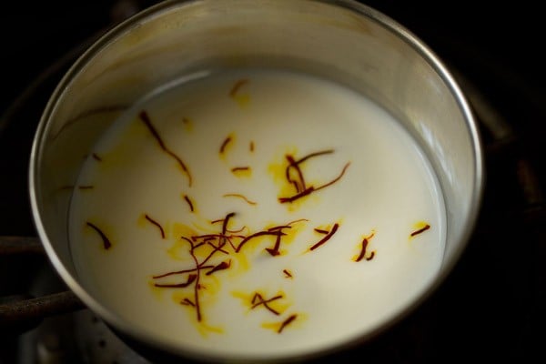 saffron strands on top of milk in a steel bowl