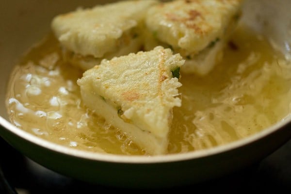 paneer sandwiches in a frying pan after being flipped; the cornstarch mixture leaves a thin golden crust on the pieces