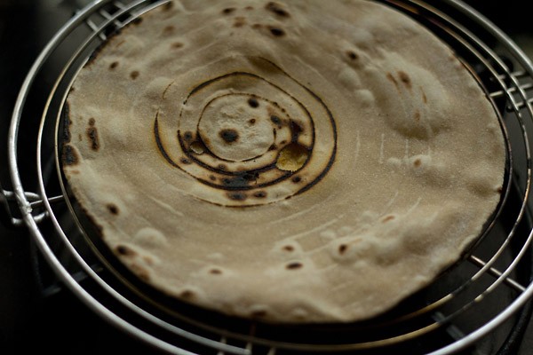 making butter roti on rack - the first side shows a circular char from the rack and flames.