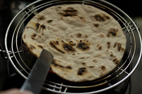 using tongs to make tandoori roti recipe on rack.