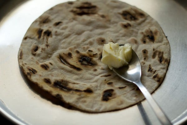 butter roti on a plate with a spoon of butter to spread on it.