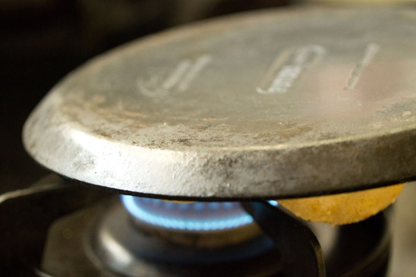 holding the tawa upside down over the flame for making tandoori roti on the stovetop.