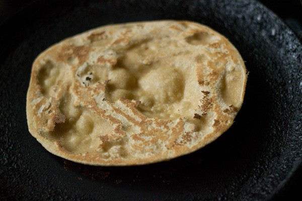 tandoori roti that has been flipped to show the underneath - there are light golden spots with the bubbled parts not showing any color.