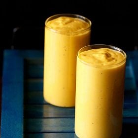 two glasses filled with fruit lassi on a dark blue tray.