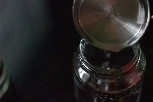 pouring vodka into jar with cut vanilla beans.