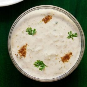 lauki ka raita in a glass bowl sprinkled with roasted cumin powder and coriander leaves on a dark green board