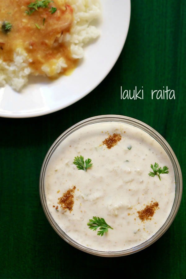 lauki ka raita in a glass bowl sprinkled with roasted cumin powder and coriander leaves on a dark green board